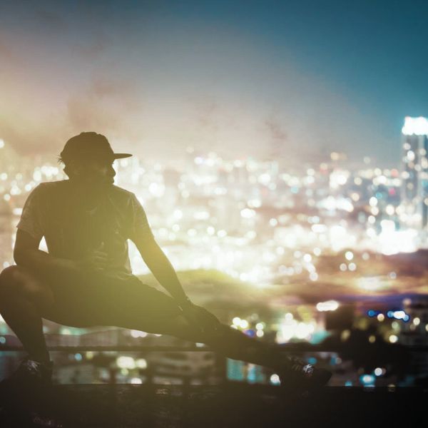 Man crouched down with a city skyline in the background at night with all the lights