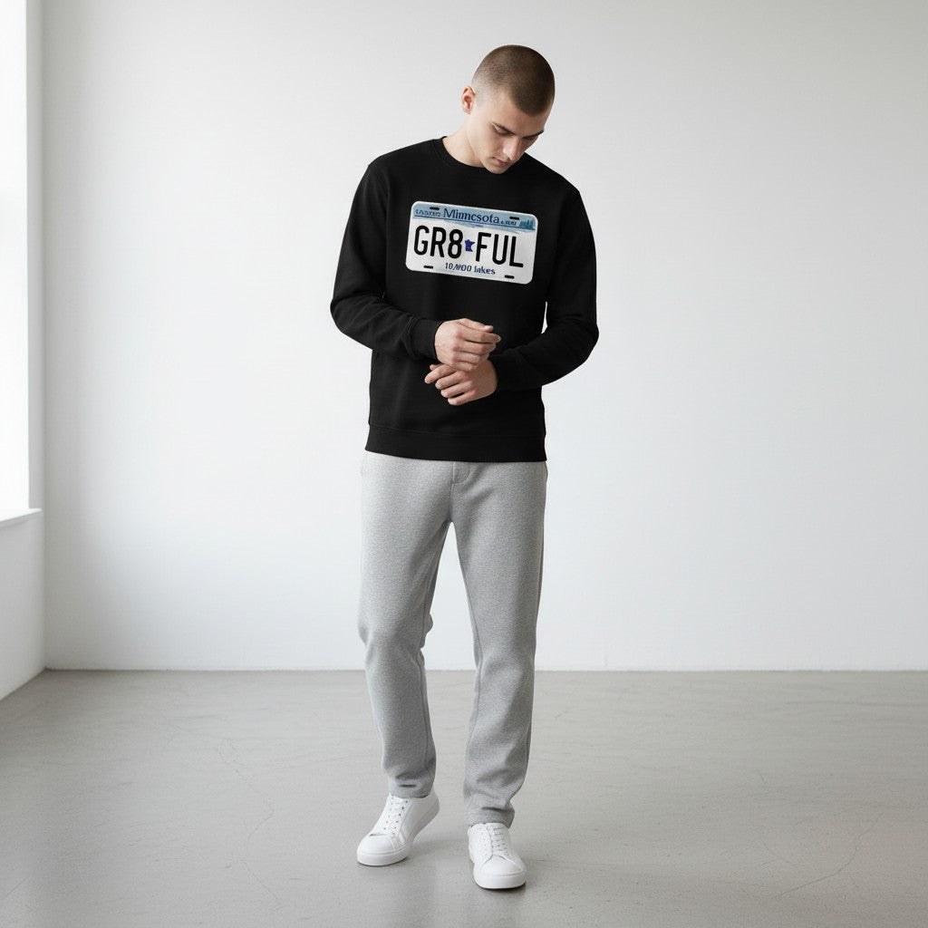 Person wearing a black long sleeve tee with a MN license plate design, standing in a minimalistic room.