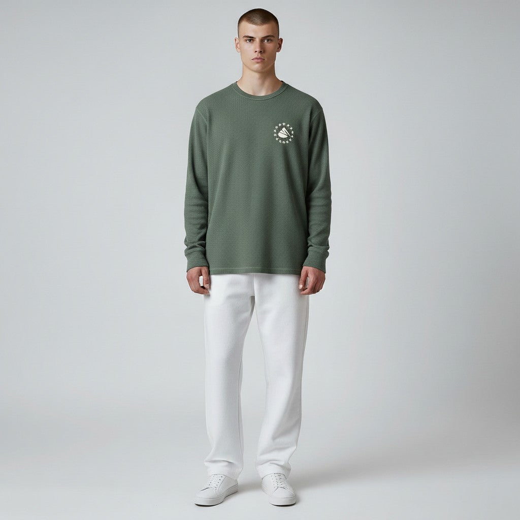 Man wearing a green long-sleeve shirt with a logo and white pants on a gray background