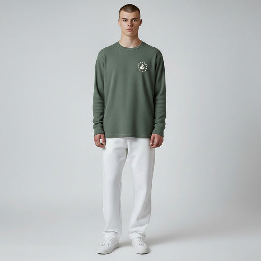 Man wearing a green long-sleeve shirt with a logo and white pants on a gray background